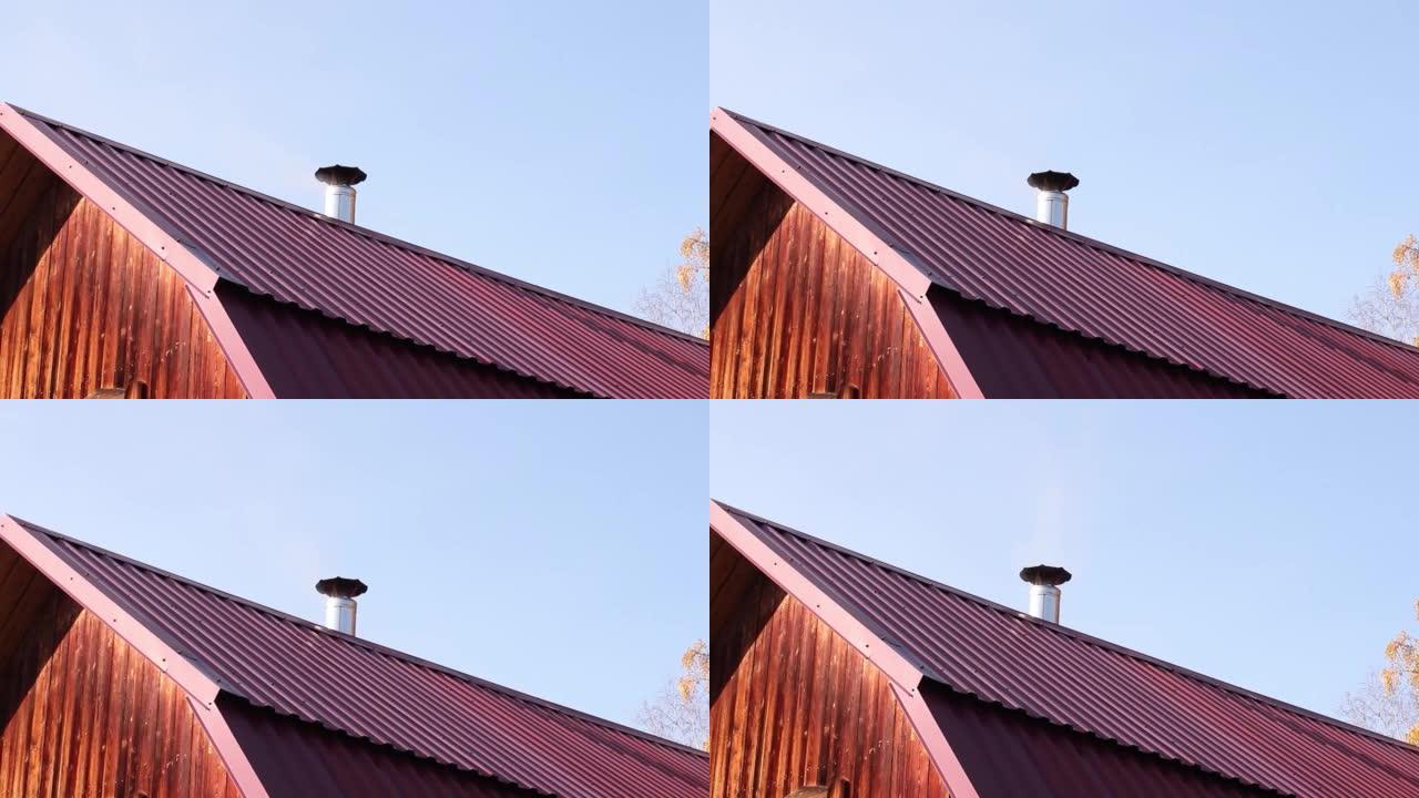 居民楼红色屋顶上的烟囱冒出淡淡的烟雾，与一棵秋树的蓝天和树枝相抵。