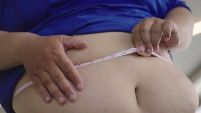 用卷尺测量腰部并轻拍腹部的超重男子的腹部特写。