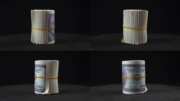 一捆100美元的钞票与在黑色背景上旋转的松紧带捆绑在一起。扭曲的钱在孤立的黑色背景上旋转。