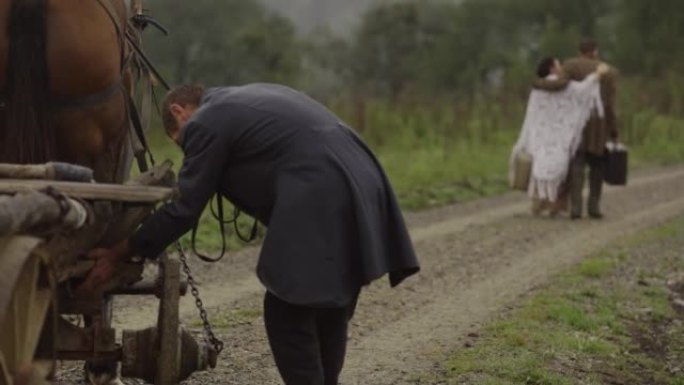 历史的重建。一个马车夫用一辆木车载着一个病人和他的妻子穿过田野。在路上行驶的马车上的木制轮子。4 k