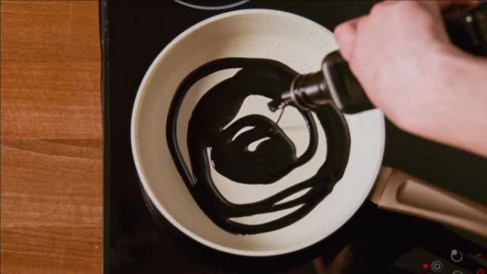 男性的手将黑油倒在白色的煎锅上。最佳镜头100fps