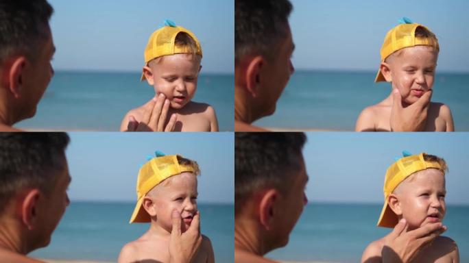 父亲在海滩上给儿子的脸上涂了防护霜。男人的手在孩子的脸上涂防晒霜。海边有防晒霜的可爱小男孩。复制空间