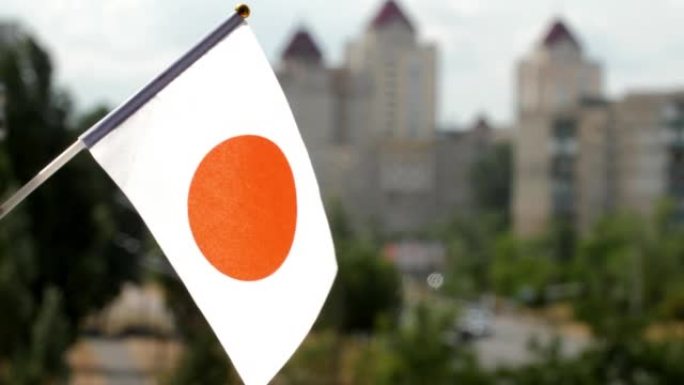 蓝天和城市街道映衬着日本国旗。挥舞日本国旗。日本的节日旗帜被太阳照亮。一面白色的旗帜，中央有一个深红