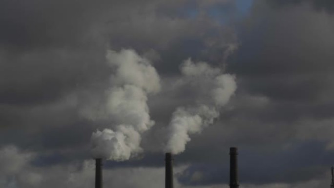 来自热电联产厂的三个烟囱的特写镜头，在多云的天空中。全球变暖、环境灾难和使用不可持续燃料的概念