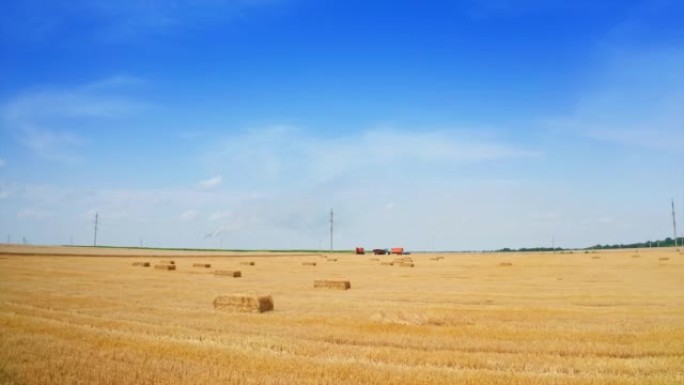 蓝色的天空与黄色的修剪过的小麦和干草形成对比。快速接近站在田间的农业机械。