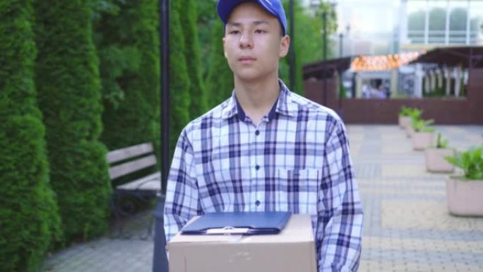 公园里戴着帽子的年轻亚洲男子送货员，手里拿着盒子