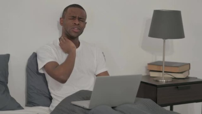 带笔记本电脑的非洲男子在床上颈部疼痛