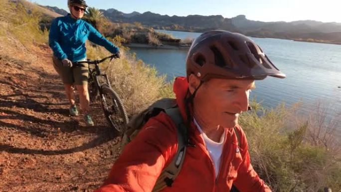 山地车手在湖边小径上推自行车的第一人称视角
