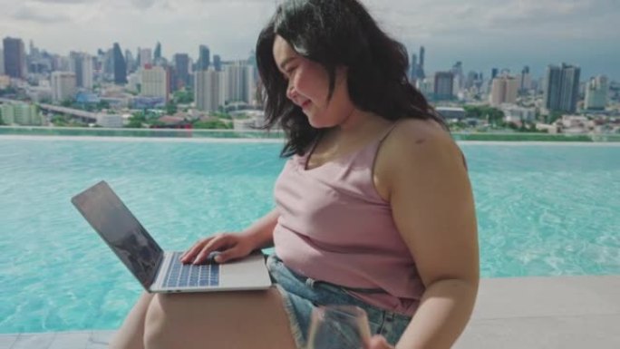 夏季，大型亚洲女性使用笔记本电脑坐在游泳池附近