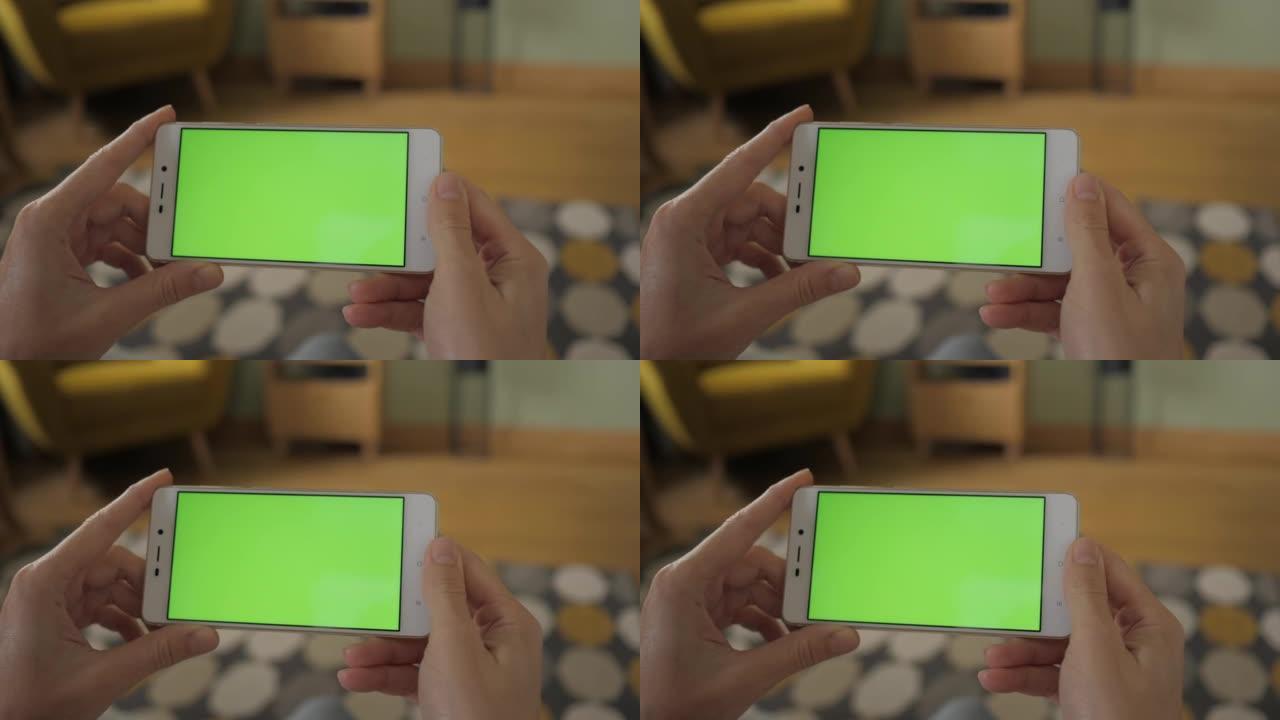 带有绿色模型屏幕色度键的手机上网观看内容视频博客点击中央屏幕。客厅女人的观点坐在椅子上使用带有绿色模