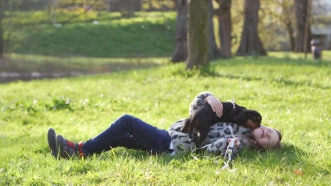 小女孩喜欢和她的小宠物狗在绿色草地上的春天公园大自然玩耍 -- 快乐的童年。狗调皮地试图舔女孩的脸