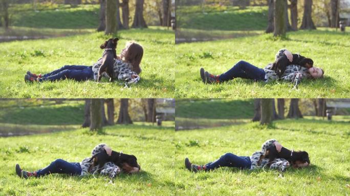 小女孩喜欢和她的小宠物狗在绿色草地上的春天公园大自然玩耍 -- 快乐的童年。狗调皮地试图舔女孩的脸