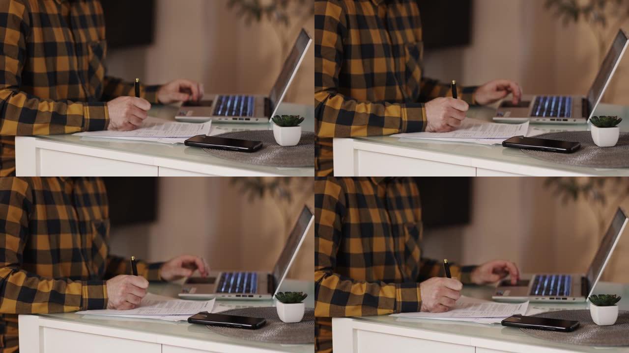 穿着方格衬衫的男子正在笔记本电脑上工作并签署文件。双手特写。远程工作、在线培训和自由职业的概念