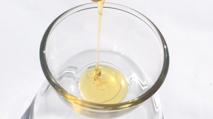 蜂蜜纯度从罐子里倒入白色背景的杯子里。颜色金色甜食蜂蜜。健康食品概念，食品，节食，有机天然蜂产品。