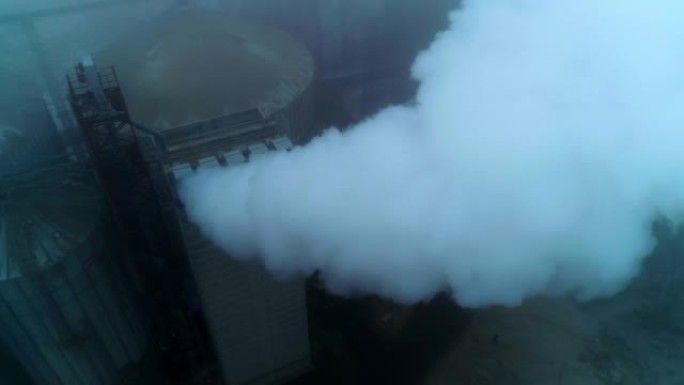 谷物升降机厂领土上的高处，管道会产生浓烟。灰色雾天背景。