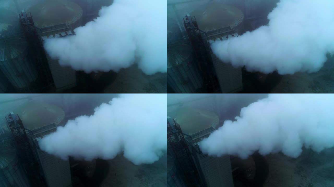 谷物升降机厂领土上的高处，管道会产生浓烟。灰色雾天背景。