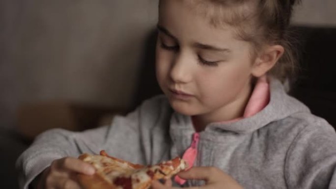 不健康的营养快餐。孩子吃午饭的肖像。面对年轻的小女孩特写。孩子吃披萨。饥饿的小女孩坐在厨房的餐桌上，