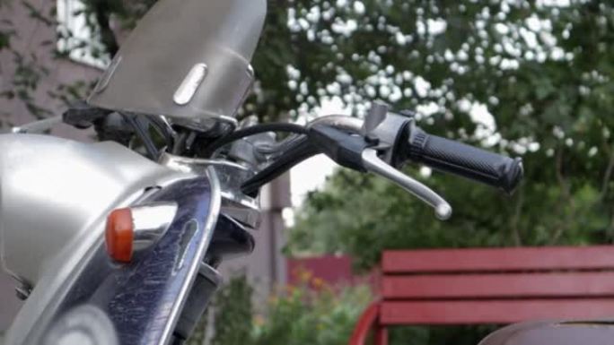 老式破旧的踏板车或迷你摩托车站在户外。流行的运输方式。带有棕色座椅的旧蓝色轻便摩托车的方向盘