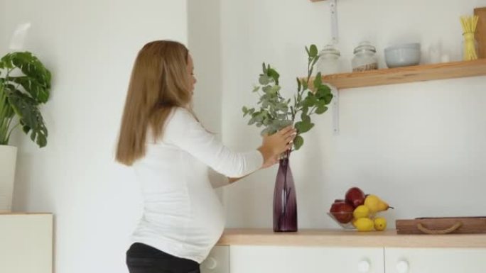 怀孕白皙的女人用花瓶里的桉树树枝装饰房子