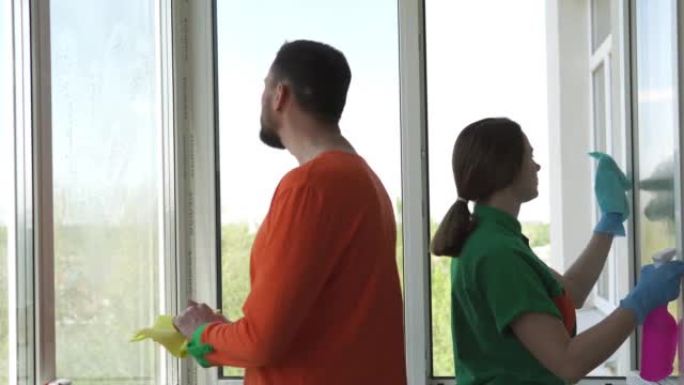 穿着工作服的清洁公司工人正在城市公寓中喷洒清洁剂并擦拭窗玻璃。用喷雾瓶清洗窗户。