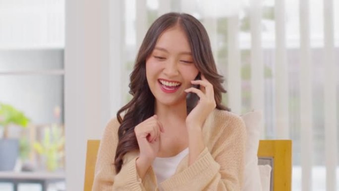 千禧一代亚洲年轻女子看着手机笑，有好消息或在家网上购物的折扣券。快乐开朗的女人看着手机app阅读消息