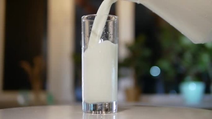 将天然牛奶从水罐倒入转盘上的玻璃杯中，将新鲜的乳制品倒入玻璃杯中，以慢动作倒入牛奶