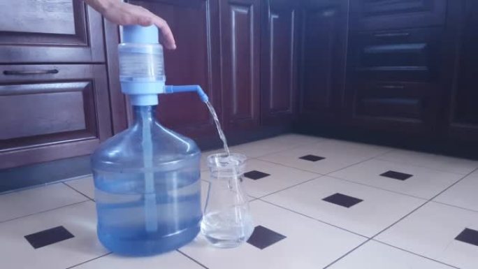 在家中用手动泵从19升塑料瓶中装满饮用水的玻璃壶