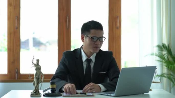 亚洲男性律师在办公室工作，在法庭桌上用木锤和女神天平与笔记本电脑。正义理念与法律良好服务咨询