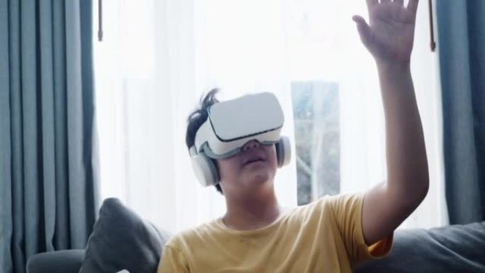 亚洲男孩玩游戏由虚拟现实男孩在沙发上靠近窗户在家里，现代生活理念。