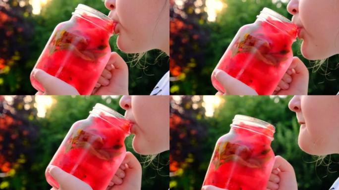 甜叶菊西瓜饮料。小女孩在夏天的花园里从杯子里喝西瓜饮料。孩子从玻璃雾蒙蒙的杯子里喝一杯红色的冷鸡尾酒
