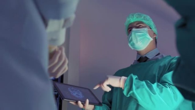 手术前，团队外科医生和助手站在一起讨论。他们穿着衣服接受手术，站在医院的手术室里。