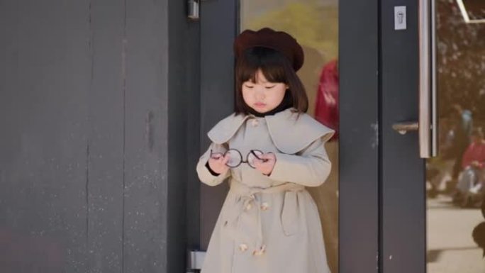 穿着灰色外套和帽子的韩国女孩在春天站在商店的玻璃门旁