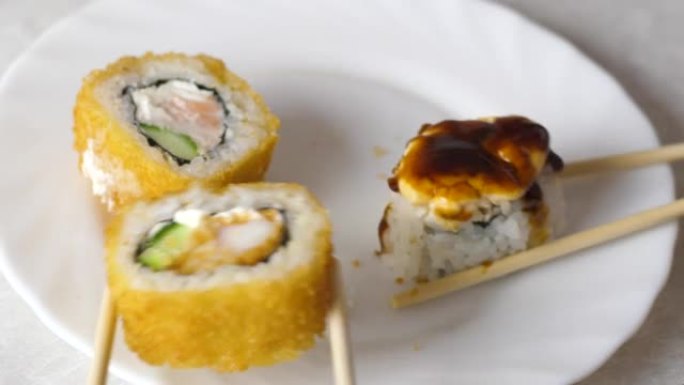 开胃的新鲜烤寿司是用筷子特写从不同侧面的盘子里取出的。日本寿司餐厅概念。寿司准备和交付。选择性聚焦