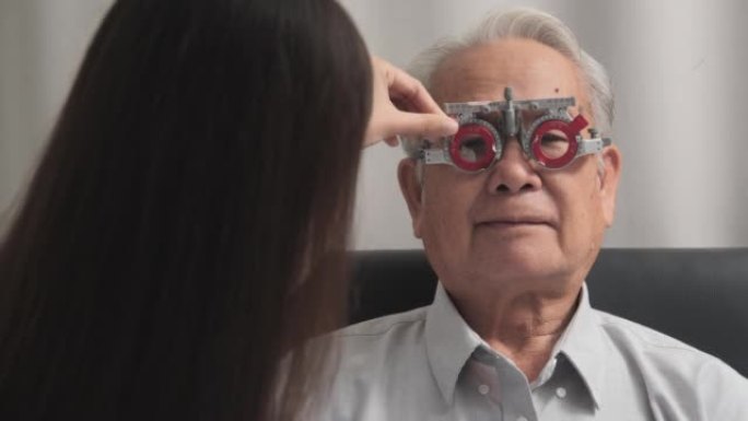 女性验光师在眼科诊所使用光学试验架检查老年男性患者的视力。