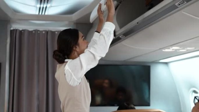 亚洲美丽的女乘务员关闭高架橱柜行李舱，以检查飞机起飞前乘客和飞机上的一群人的安全。航空公司概念。