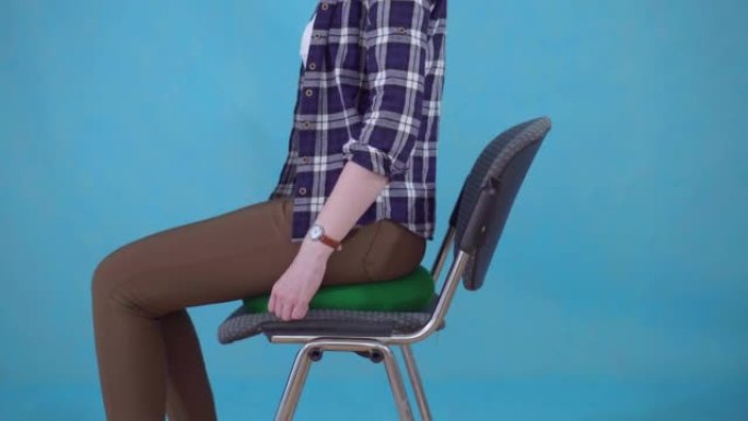 穿着衬衫的女人坐在蓝色背景的椅子上的矫形枕头上，痔疮的概念特写
