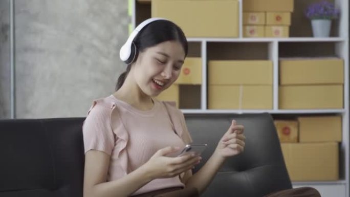 一个戴着耳机的年轻亚洲妇女可以在家里的沙发上愉快地听音乐。