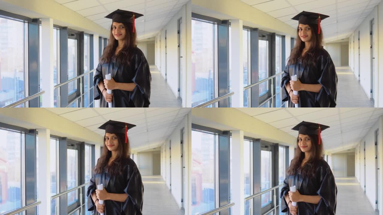 披风的巴基斯坦女毕业生手里拿着文凭站着，微笑着