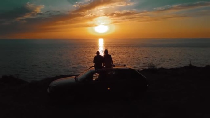 在海上日落时坐在汽车上的一男一女的无人机视图