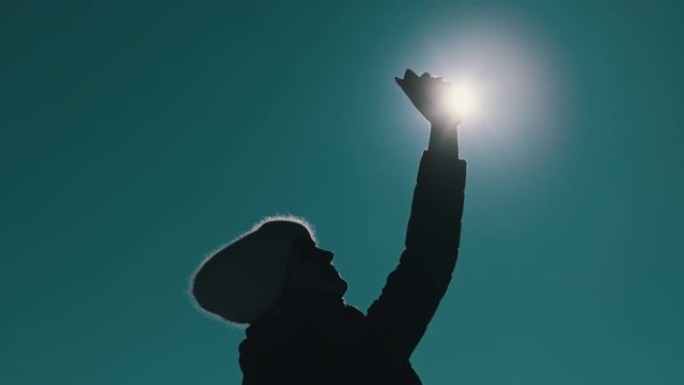 反对太阳的女人举起手机高高的手来捕捉冬天丢失的信号