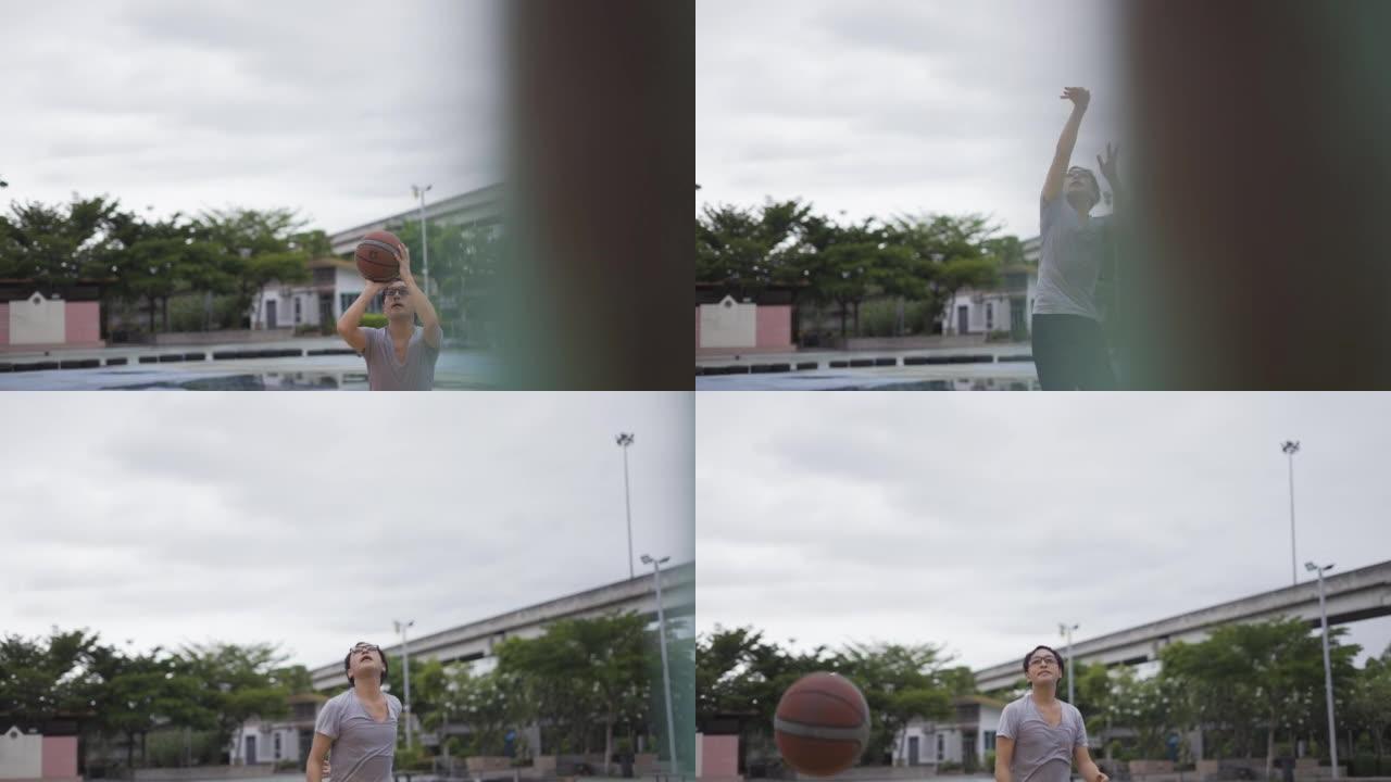 亚洲男子打球运球，将篮球射入篮筐，在日落时在户外球场上玩得很开心。男子篮球运动员在野外练习篮球。运动