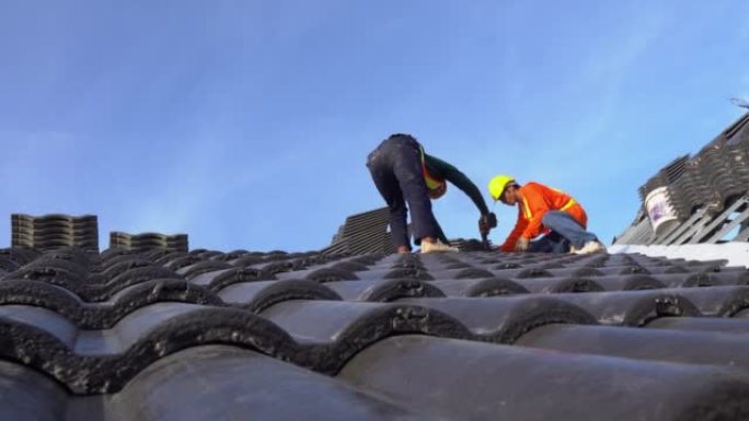 两名穿着安全服的屋顶工人正在团队合作，在建筑工地安装瓷砖屋顶的房屋屋顶。团队合作理念。