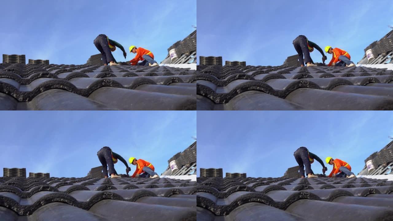两名穿着安全服的屋顶工人正在团队合作，在建筑工地安装瓷砖屋顶的房屋屋顶。团队合作理念。