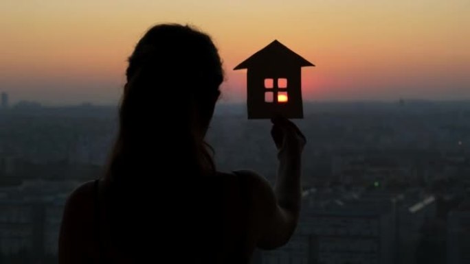 梦幻的女人站在窗前，手里拿着一个房子的小模型
