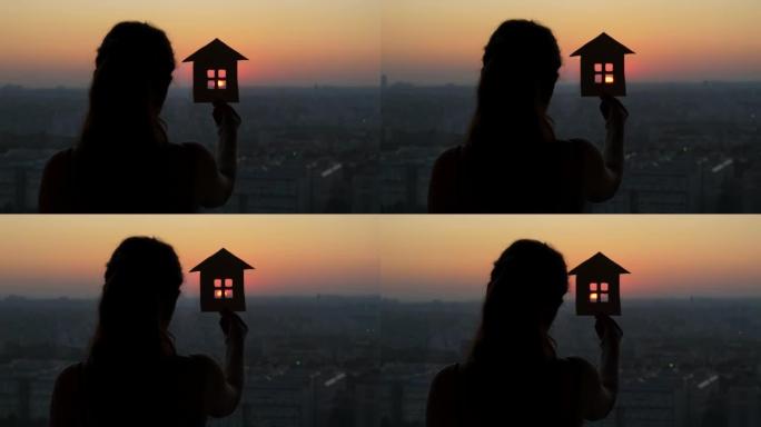 梦幻的女人站在窗前，手里拿着一个房子的小模型