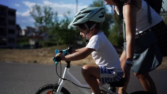 活跃的小男孩在阳光明媚的日子里和妈妈一起在外面学习骑自行车。在阳光明媚的日子里，孩子在父母的帮助下学
