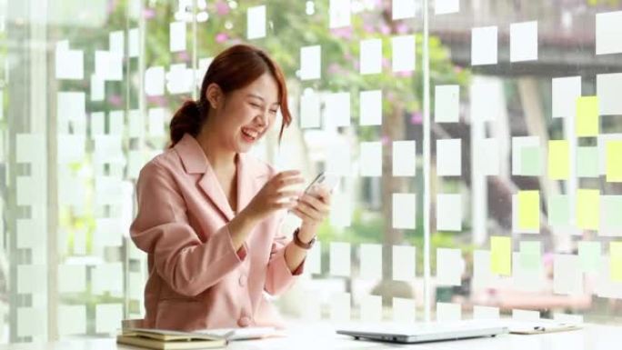 一位亚洲女商人坐在一家公司的私人办公室里，她看着手机上的数据，当她看到公司的利润数据时，她看起来很高