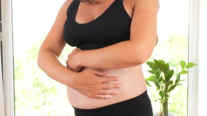 一个怀孕的女孩在她的肚子上涂上妊娠纹乳膏。