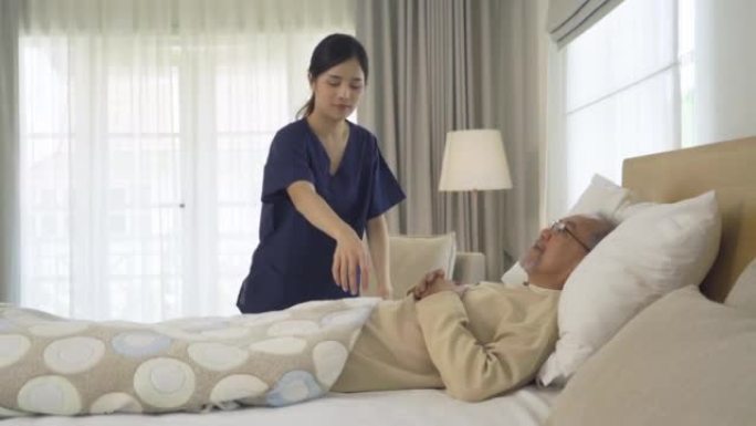 快乐的女人护士，女儿为生病的老年老年患者盖了毯子，躺在床上在家里的卧室或房子里接受医疗和保健治疗。亚