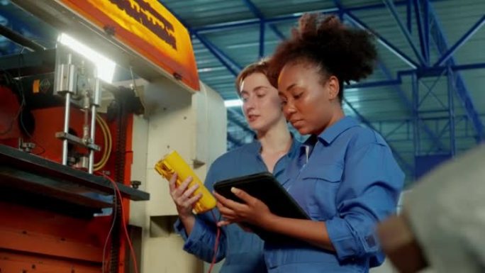 Mix race穿着安全服的年轻女工程师正在一起工作，在夜班的工厂生产线中使用检流计检查和测量机器的